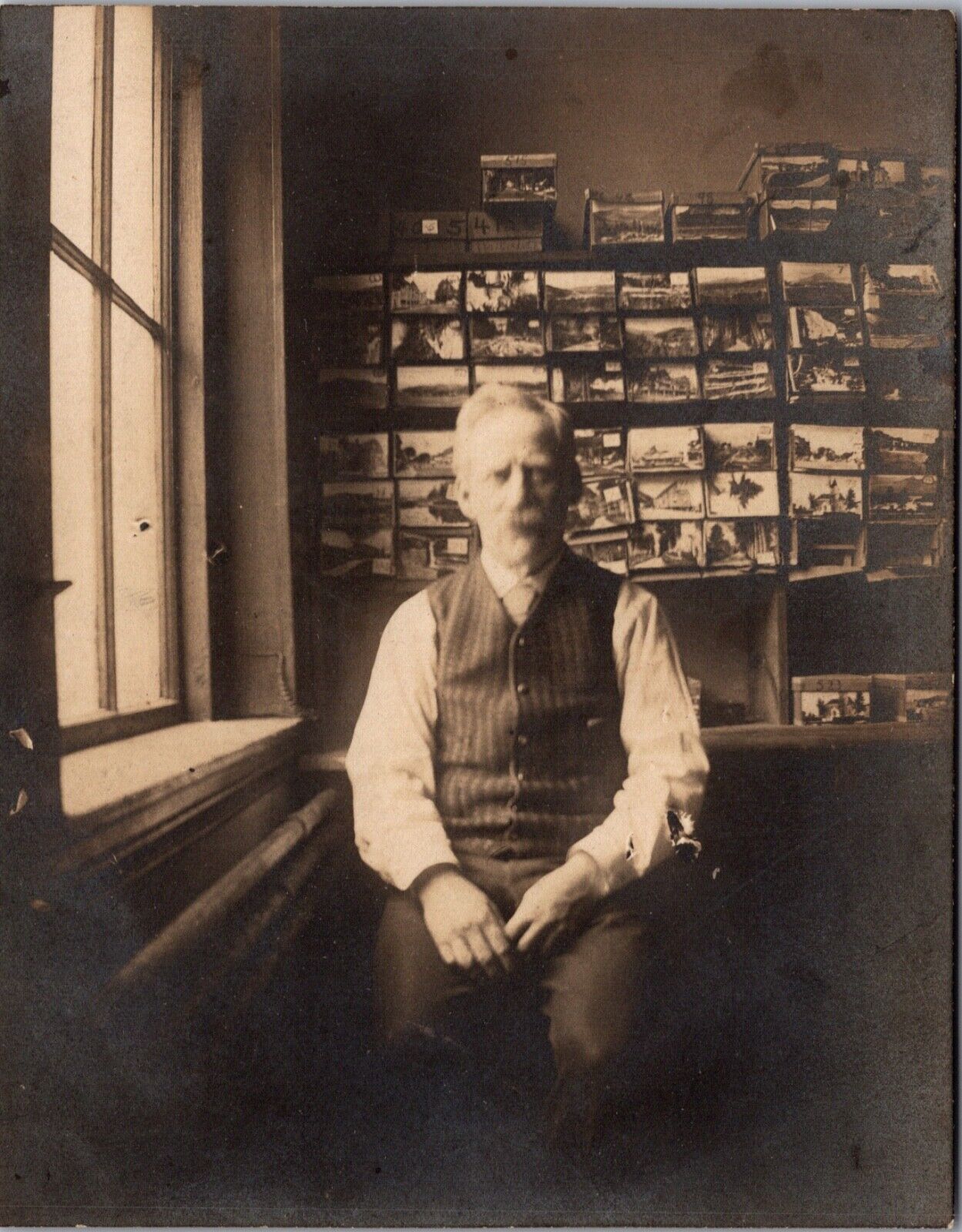 Snapshot Photograph of a Man with a Wall and Boxes of Postcards Behind Him